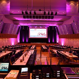 Der Blick auf unsere Bühne im Maria-Theresia-Saal. Der Raum ist leuchtend lila angestrahlt. Foto: Bernhard Weizenegger