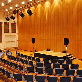 Blick auf den Marie-Antoinette-Saal von der Seite. Zu sehen ist die Bühne und vordere Stuhlreihen sowie einige Scheinwerfer, die die Bühne von oben beleuchten. Foto: Contrast Marketing für Stadt Günzburg